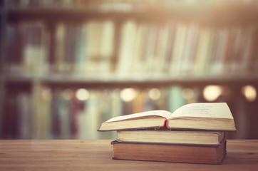 back to school concept. stack of books over wooden desk in front of library and shelves with books.