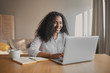 © Anatoliy Karlyuk - Cheerful young African American woman copywriter sitting in front of open laptop with mug and copybook on desk, feeling inspired, working on new motivation article. People, occupation and creativity