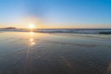 Fototapeta Nowy Jork - Sunrise star burst over the beach with shiny wet sand in the foreground, NSW, Australia