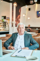 Wall Mural - Portrait of contemporary senior businessman looking away pensively while working at table in cafe during coffee break