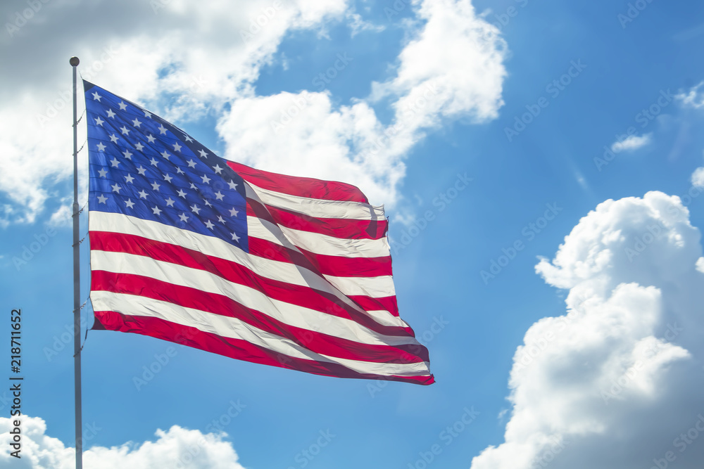 Waving American flag against a bright blue sky with fluffy white clouds ...