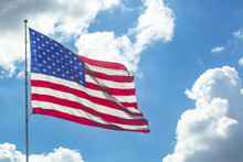 Waving American Flag Against A Bright Blue Sky With Fluffy White Clouds