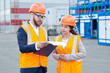 © Seventyfour - Waist up portrait of two modern factory workers wearing hardhats discussing production over clipboard outdoors, copy space