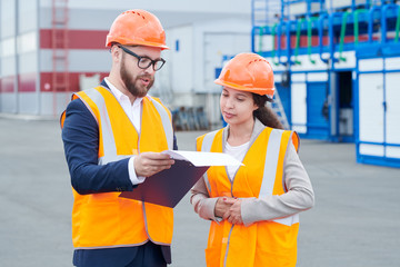 Wall Mural - Waist up portrait of two modern factory workers wearing hardhats discussing production over clipboard outdoors, copy space