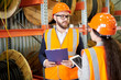 © Seventyfour - Portrait of modern bearded businessman wearing hardhat listening to factory employee while standing in workshop and holding clipboard, copy space