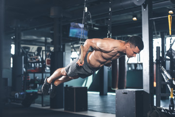 Shredded guy is feeling tension while exercising with gymnastic equipment. He is straightening all body and bringing it to parallel to floor. Male is holding handles and looking down