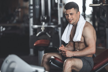 cheerful shirtless man is resting after workout with machines and weights. he is sitting on bench an
