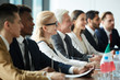 © pressmaster - Row of international politicians in formalwear sitting by long table at conference and listening to introduction at the beginning