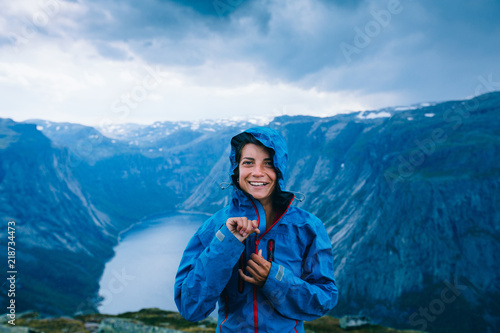 Fotografía Happy woman zip up blue sportive jacket before rain, get ready for adventure and smiling in cliff during trip Norway