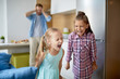 © pressmaster - Two cute girls shouting loudly during their home play on background of their father covering ears