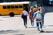 Rear view of group of teen scholars walking to school bus by parking