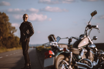 Canvas Print - smiling man standing on road with classical motorcycle, selective focus