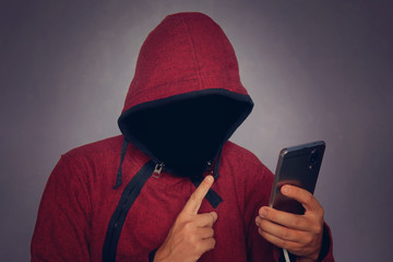 Silhouette of a man in a hood on a black background, his face is not visible, the hacker is holding the phone in his hands. The concept of a criminal, incognito, mystery, secrecy, anonymity.