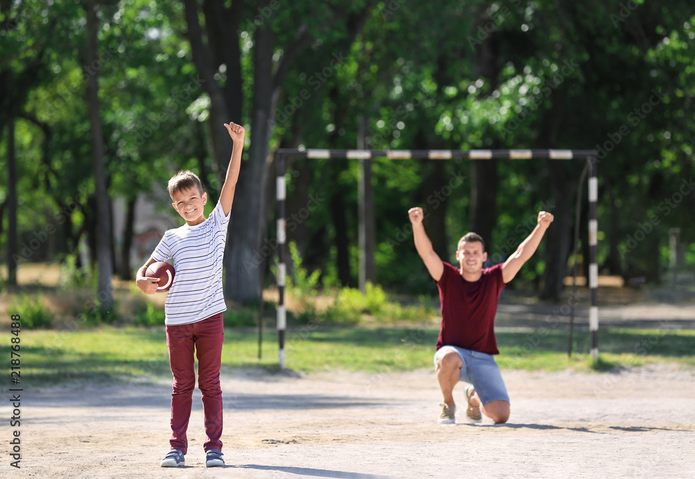 Little boy with his dad playing rugby on pitch