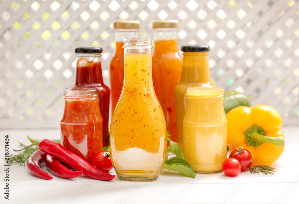 Glassware with different tasty sauces and vegetables on white table