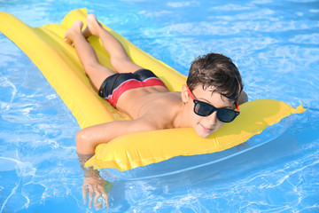 cute little boy resting on inflatable mattress in swimming pool