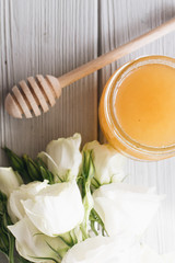 Honey dipper, honey and white flowers on wooden board