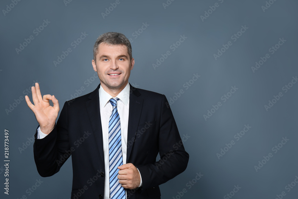 Handsome businessman showing OK gesture on grey background