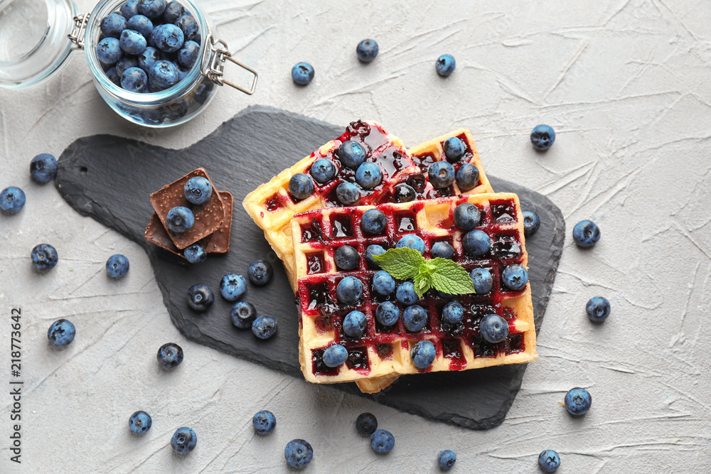 Delicious waffles with blueberries and jam on slate plate