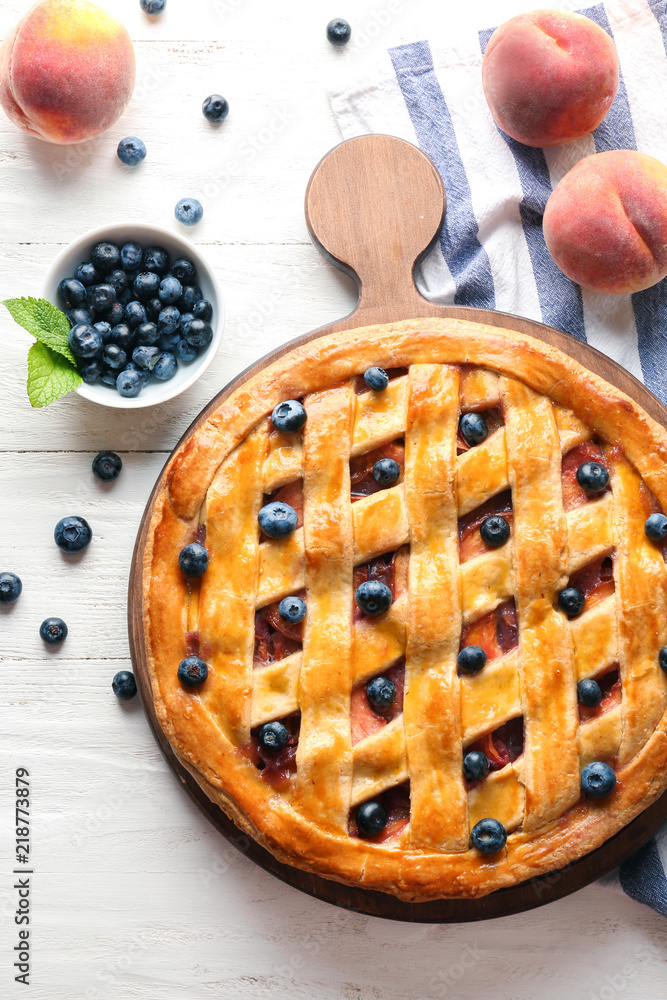 Board with delicious peach pie and blueberry on white wooden table