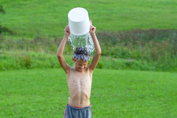 Little boy pouring cold water on his head outdoors