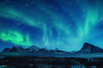 Northern Lights, Aurora Borealis shining green in night starry sky with star tracks at winter Lofoten Islands, Norway