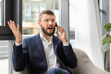 Wall Mural - Emotional businessman talking on phone in office