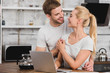 © LIGHTFIELD STUDIOS - happy boyfriend hugging girlfriend in kitchen while she working with laptop and they looking at each other