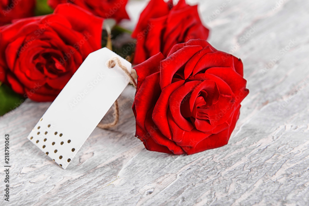 Beautiful bouquet of red roses and tag on light background