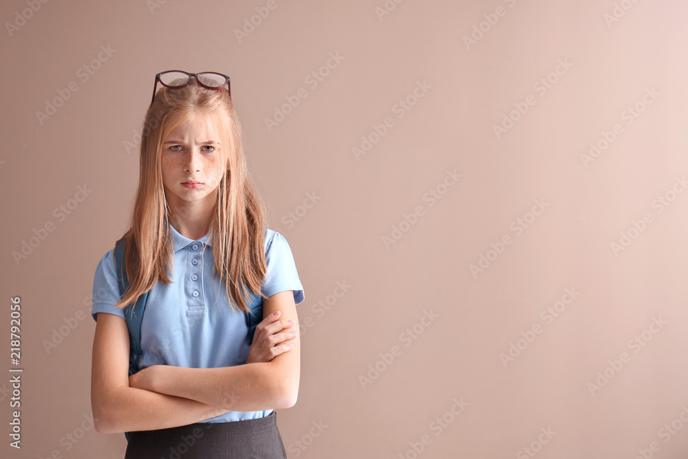 Displeased schoolgirl on color background