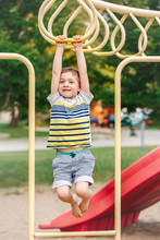 Young Caucasian Boy Hanging On Monkey Bars In Park On Playground. Active Preschool Child Doing Exercises Sport. Healthy Happy Childhood.