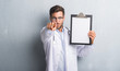 © Krakenimages.com - Handsome young doctor man over grey grunge wall holding clipboard pointing with finger to the camera and to you, hand sign, positive and confident gesture from the front