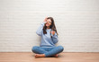 © Krakenimages.com - Young brunette woman sitting on the floor drinking glass of water with happy face smiling doing ok sign with hand on eye looking through fingers