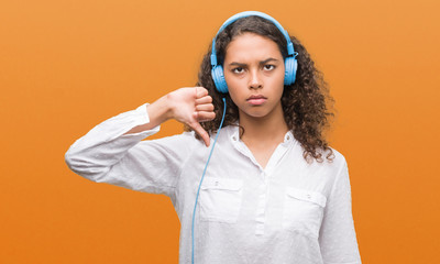 Young hispanic woman wearing headphones with angry face, negative sign showing dislike with thumbs down, rejection concept