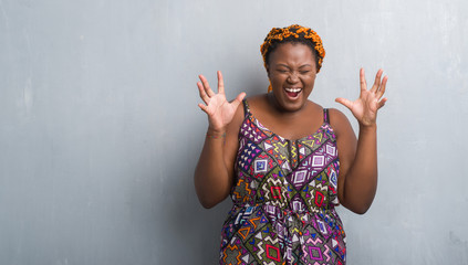 Canvas Print - Young african american woman over grey grunge wall wearing orange braids celebrating mad and crazy for success with arms raised and closed eyes screaming excited. Winner concept