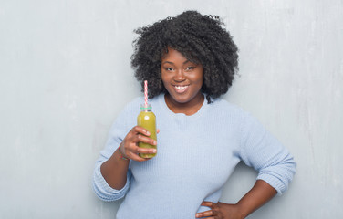 Poster - Young african american woman over grey grunge wall drinking detox green juice with a happy face standing and smiling with a confident smile showing teeth