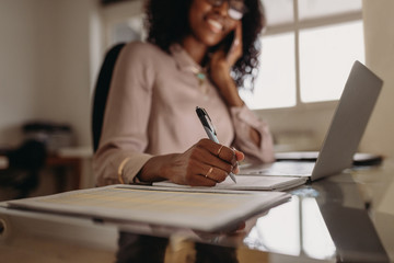 Woman making notes working on laptop at home