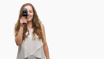 Wall Mural - Young blonde woman holding super 8 video camera with a happy face standing and smiling with a confident smile showing teeth