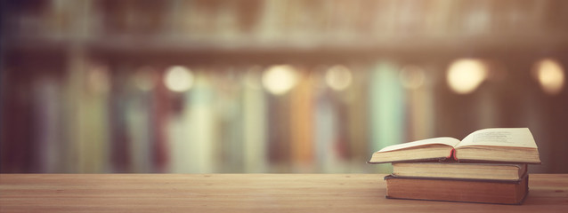 back to school concept. stack of books over wooden desk in front of library.