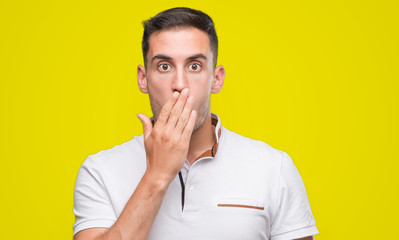 Canvas Print - Handsome young casual man wearing white t-shirt cover mouth with hand shocked with shame for mistake, expression of fear, scared in silence, secret concept