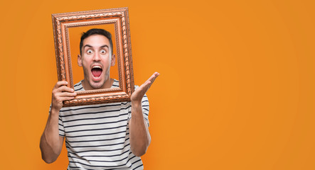 Poster - Handsome young man looking through vintage art frame very happy and excited, winner expression celebrating victory screaming with big smile and raised hands