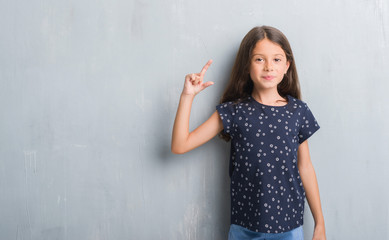 Wall Mural - Young hispanic kid over grunge grey wall smiling and confident gesturing with hand doing size sign with fingers while looking and the camera. Measure concept.