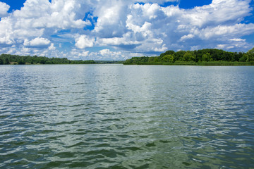 Wall Mural - A beautiful image of landscape from the center of the river, surrounded by trees and reeds on the shore and distant horizon against the blue sky in clouds. Reflection, water, tourist destination