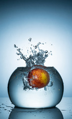 An apple dropped into fish bowl with water splash.