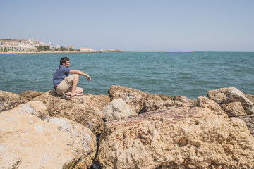 Wall Mural - man looking at the sea on the stones of the shore