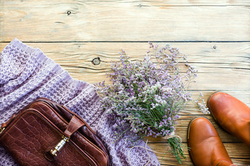 Red shoes, purple bouquet, sweater, scarf and leather bag on a vintage wooden background, concept