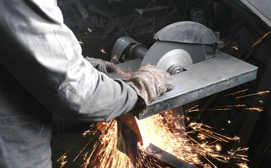 Cutting of metal. Closeup men's hands cutting metal with a circular saw. Sparks fly to the side.