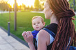 © Artem - Young happy mom with baby son in ergo backpack walking in the Park. Concept of modern parents