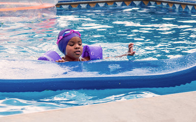 Wall Mural - A young African girl is enjoying swimming at summer time