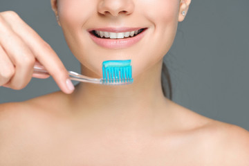 cropped shot of smiling woman holding tooth brush with tooth paste isolated on grey